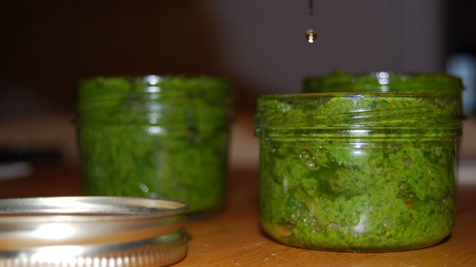 Pots de pesto au basilic avec un filet d'huile qui coule dessus.